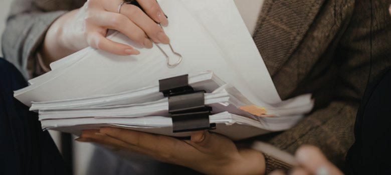 Eine Person hält einen dicken Stapel Dokumente, die mit schwarzen Foldback-Klammern sortiert sind