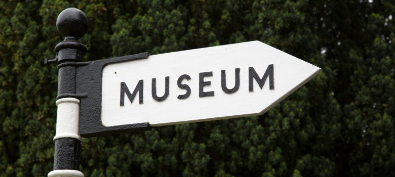 Aufnahme eines Straßenschildes mit schwarz-weißem Pfosten mit der Aufschrift 'Museum', das nach rechts zeigt