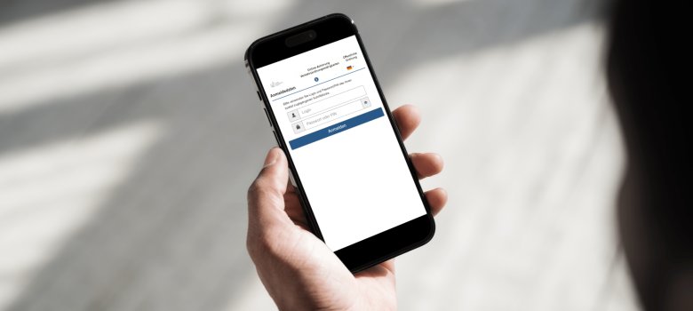 Aktuelles - 7 Eine Hand hält ein Smartphone, auf dessen Display eine mobile Anmeldeseite für die Online-Anhörung von Verkehrsordnungswidrigkeiten mit Eingabefeldern für Login und Passwort zu sehen ist