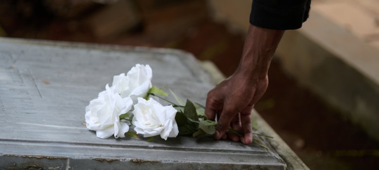 Eine Hand legt drei weiße Rosen auf eine steinerne Grabplatte