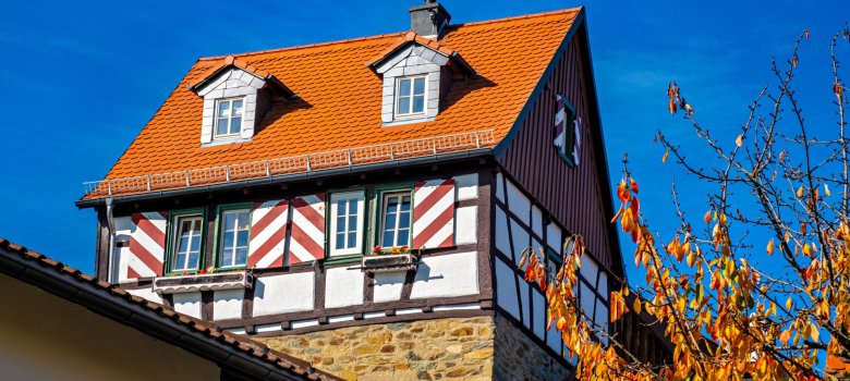 Ein mehrstöckiges Fachwerkhaus auf einem Bruchsteinsockel, das durch rot-weiß gestreifte Fensterläden auffällt