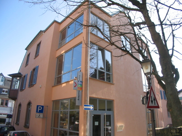 Die Außenansicht des modernen Erweiterungsbaus der StadtBücherei Kronberg mit großen Fensterfronten, lachsfarbener Fassade und dem bunten Bücherei-Hinweisschild.