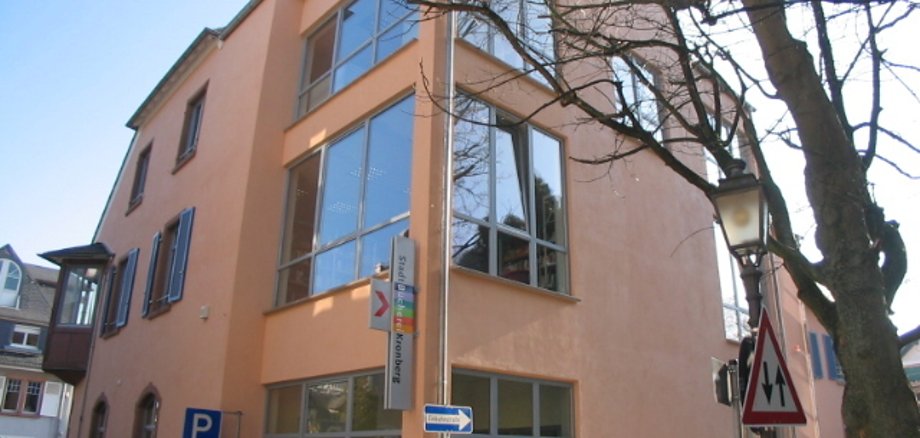 Die Außenansicht des modernen Erweiterungsbaus der StadtBücherei Kronberg mit großen Fensterfronten, lachsfarbener Fassade und dem bunten Bücherei-Hinweisschild.