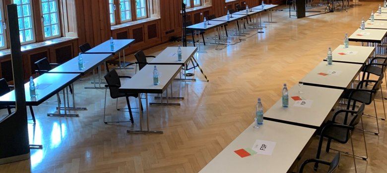 Ein historisch anmutender Saal mit Holzvertäfelung, in dem Tische für eine Sitzung (mit Namensschildern wie „FDP“) aufgestellt sind