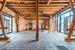 Eine große, historische Event-Scheune mit freigelegtem Holzgebälk, alten Steinfassaden, einem Ziegelboden und modernen Glaselementen an den Seitenwänden.