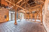 Eine große, historische Event-Scheune mit freigelegtem Holzgebälk, alten Steinfassaden, einem Ziegelboden und modernen Glaselementen an den Seitenwänden.