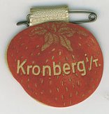 Anstecknadel mit einer roten Erdbeere aus Karton oder Leder, auf der in goldener Schrift Kronberg i/T. steht.