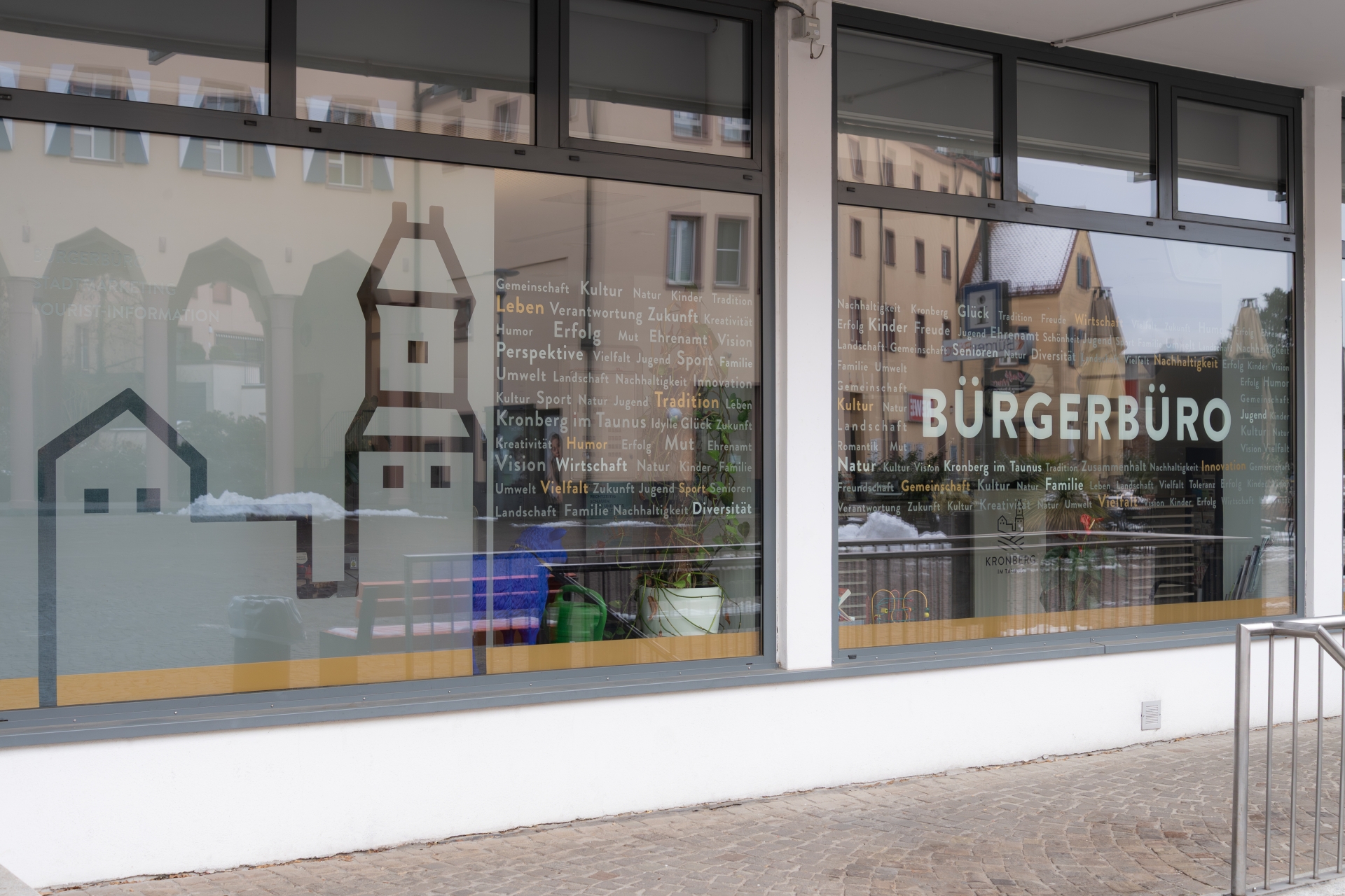 Außenansicht des Bürgerbüros Kronberg; die Fensterscheiben sind mit dem Stadtlogo und einer Wortwolke aus Begriffen wie Gemeinschaft, Kultur und Zukunft gestaltet