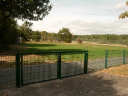 Ein eingezäunter Fußballplatz mit grünem Metalltor im Vordergrund