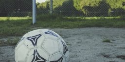 Ein Fußball liegt im Vordergrund vor einem Fußballtor auf einem staubigen Platz
