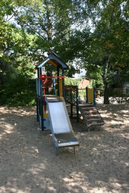 Ein bunter Spielturm mit Rutsche und kleiner Kletterwand in einer Sandkiste