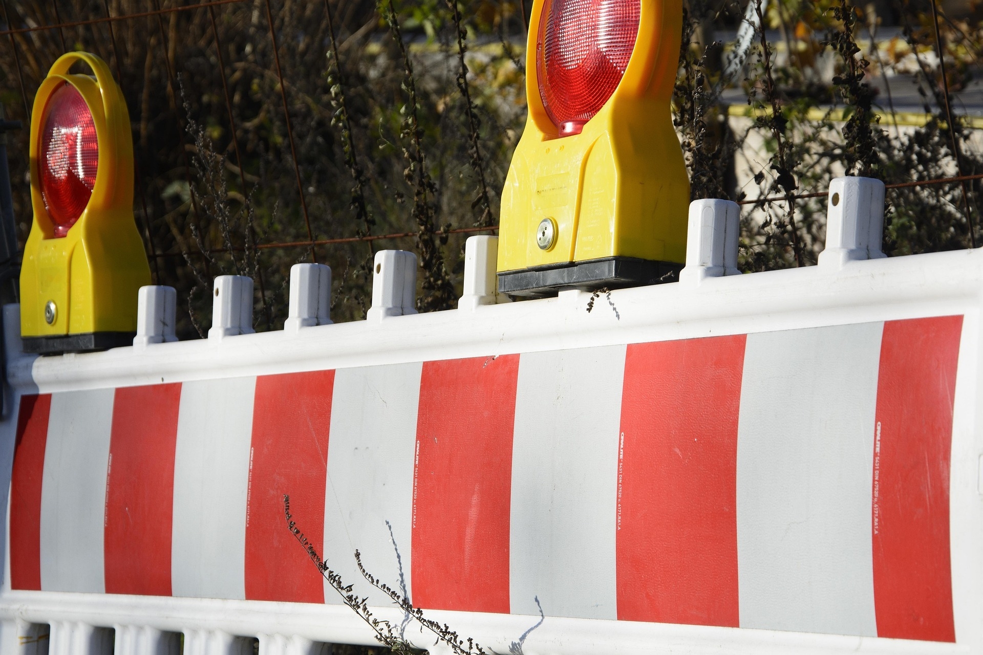 Sicherheitsabsperrung im Außenbereich: Weißer Schrankenzaun mit roten Reflektorstreifen und gelben Baustellenlampen im hellen Tageslicht