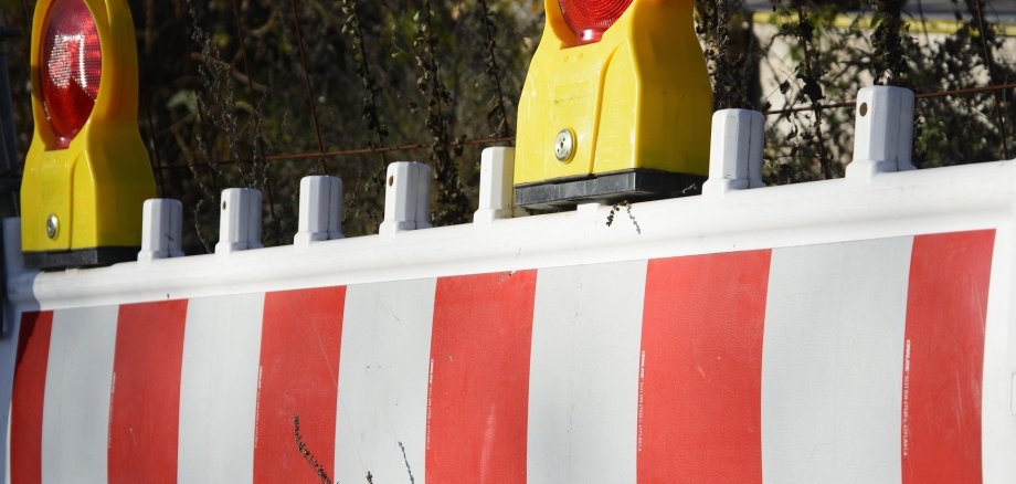 Sicherheitsabsperrung im Außenbereich: Weißer Schrankenzaun mit roten Reflektorstreifen und gelben Baustellenlampen im hellen Tageslicht