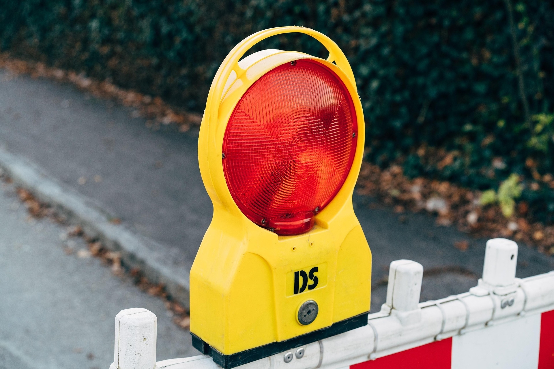 Gelbe Baustellen-Warnleuchte mit roter runder Linse, montiert auf einer rot-weiß gestreiften Absperrschranke an einem Gehweg