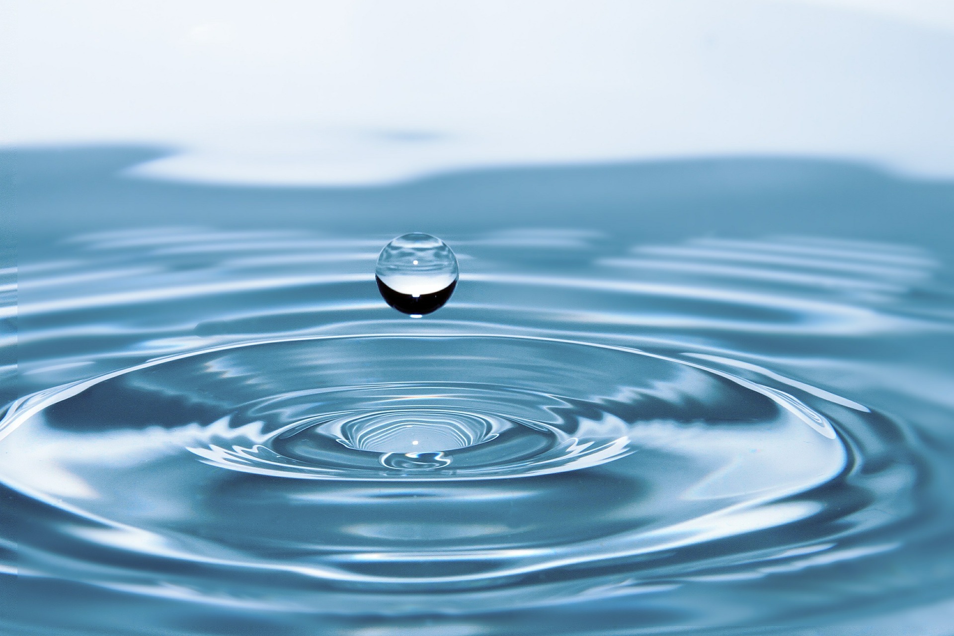 Makroaufnahme eines einzelnen Wassertropfens kurz vor dem Aufprall auf eine spiegelnde Wasseroberfläche
