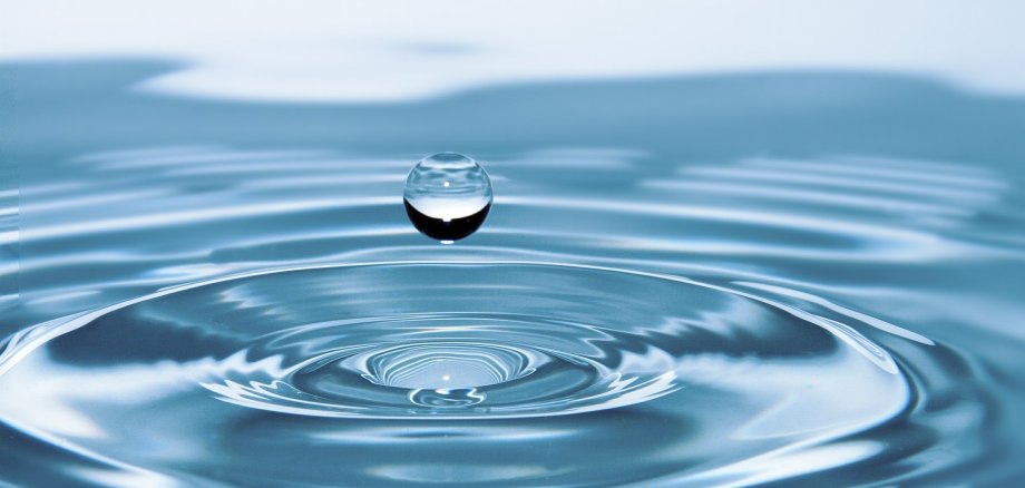 Makroaufnahme eines einzelnen Wassertropfens kurz vor dem Aufprall auf eine spiegelnde Wasseroberfläche
