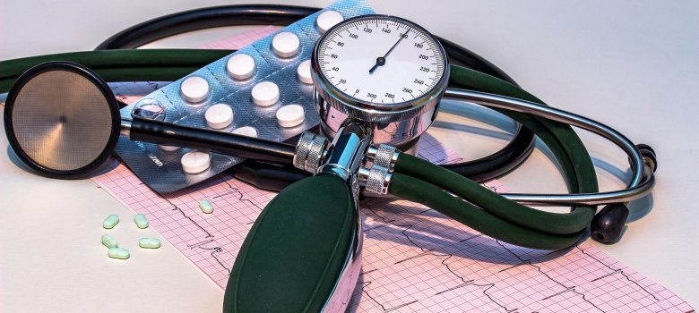 Medizinische Ausrüstung: Analoges Blutdruckmessgerät, Stethoskop, Tabletten und ein EKG-Ausdruck auf weißem Untergrund