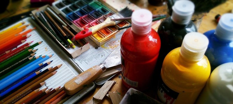 Farben in Tuben (rot, gelb, schwarz, blau und weiß, Bunstiffte in allen Farben und ein Wasserfarbkasten, auf dem ein Pinsel liegt