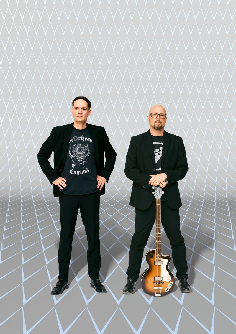 hessische Mundart-Duo Das hessische Mundart-Duo Tilman Birr und Elis C. Bihn in schwarzen Sakkos mit einer E-Gitarre vor grauem Rauten-Hintergrund.