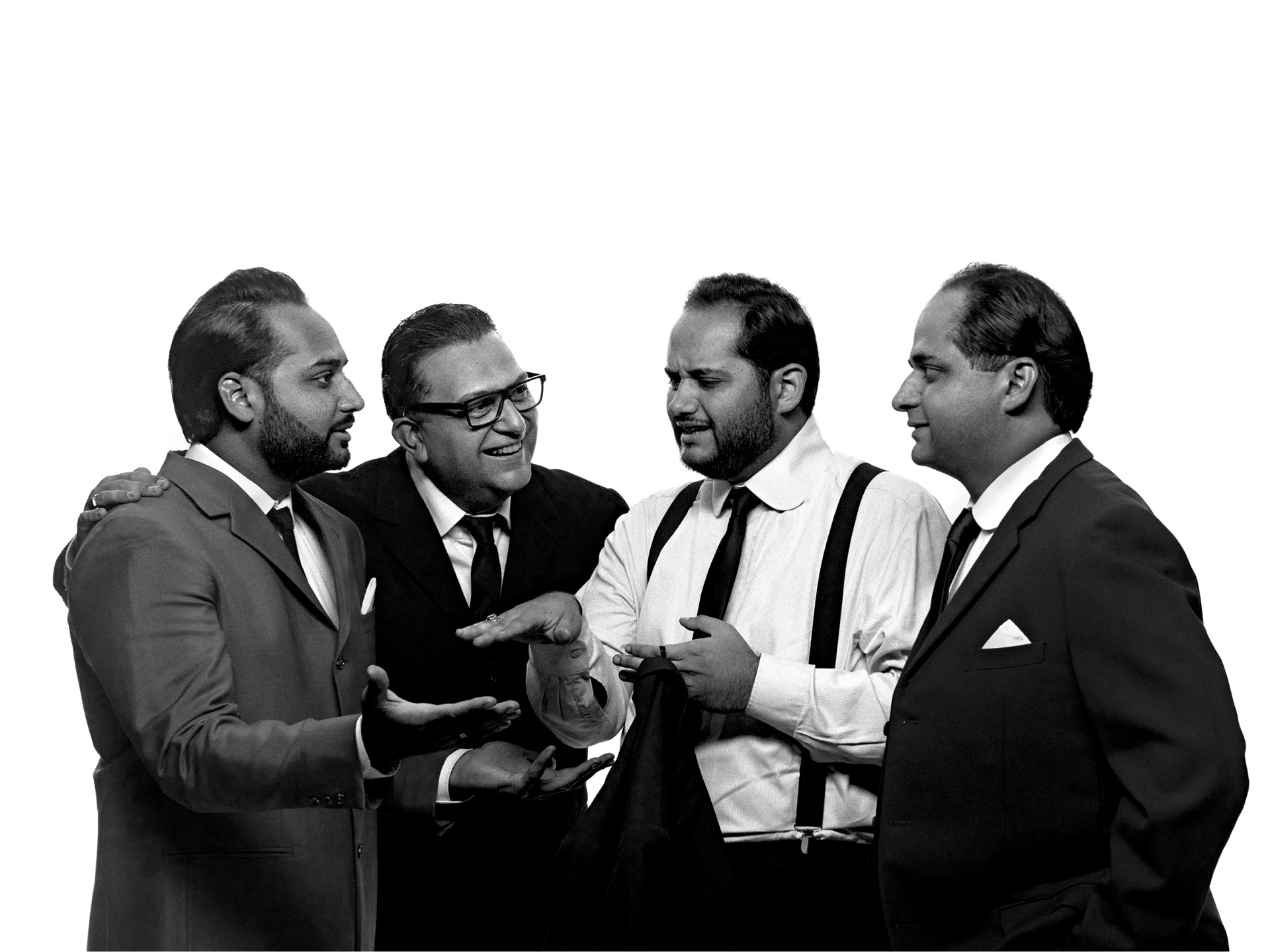 Janoska Ensemble Schwarz-Weiß-Fotografie der vier Musiker des Janoska Ensemble vor rein weißem Hintergrund. Die Männer stehen eng zusammen, tragen elegante Anzüge und unterhalten sich gestenreich. Ein Musiker trägt Brille und lacht, ein anderer hat sein Sakko abgelegt und trägt gut sichtbare Hosenträger über dem weißen Hemd.